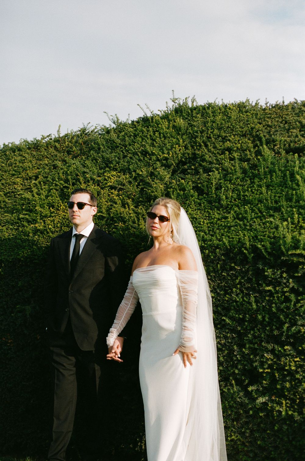 A bride and groom pose against a green hedge backdrop in a series of candid wedding photos. Paris editorial elopement photographer.