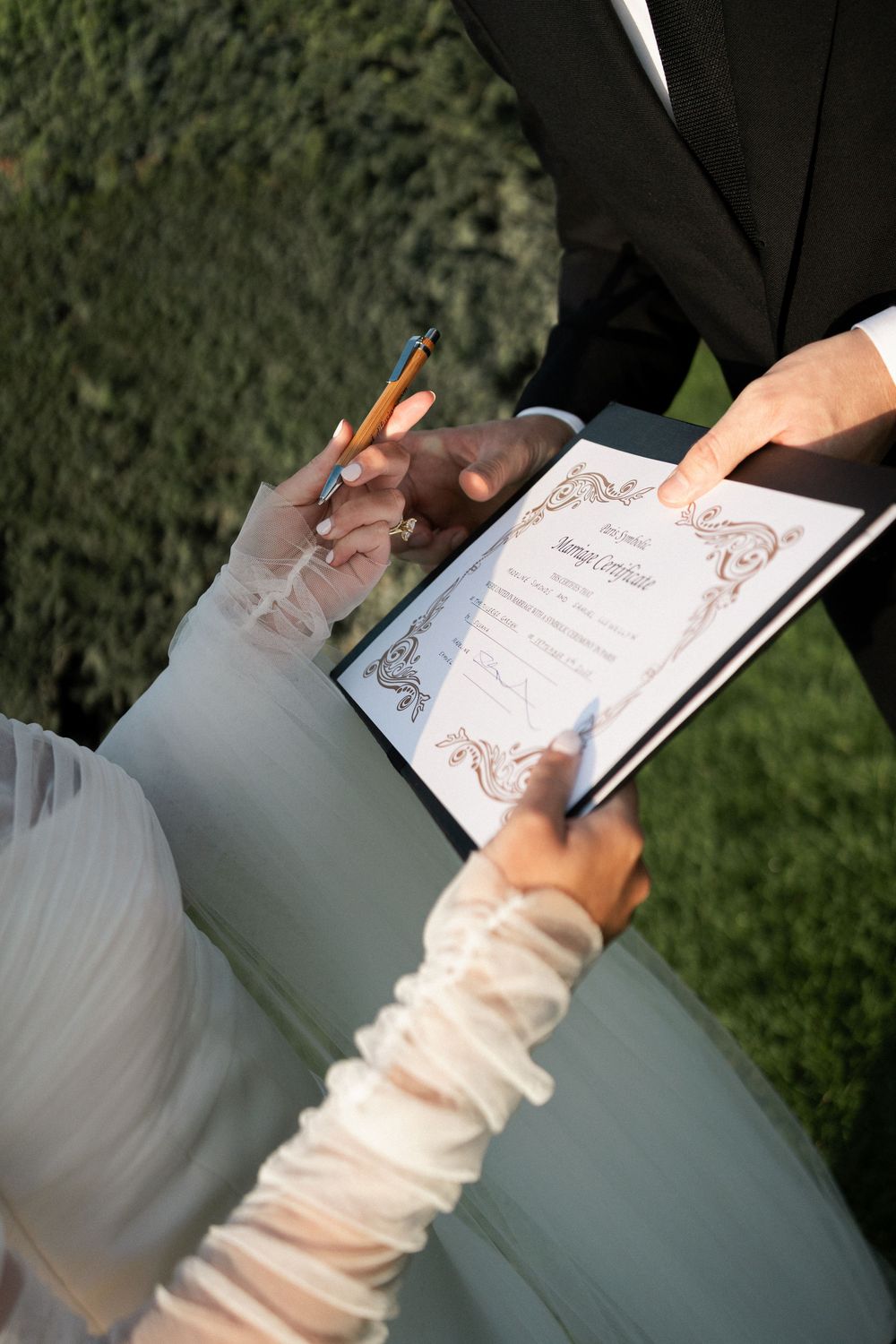 Close-up view of hands signing documents with a pen on a reflective surface. Paris editorial elopement photographer.