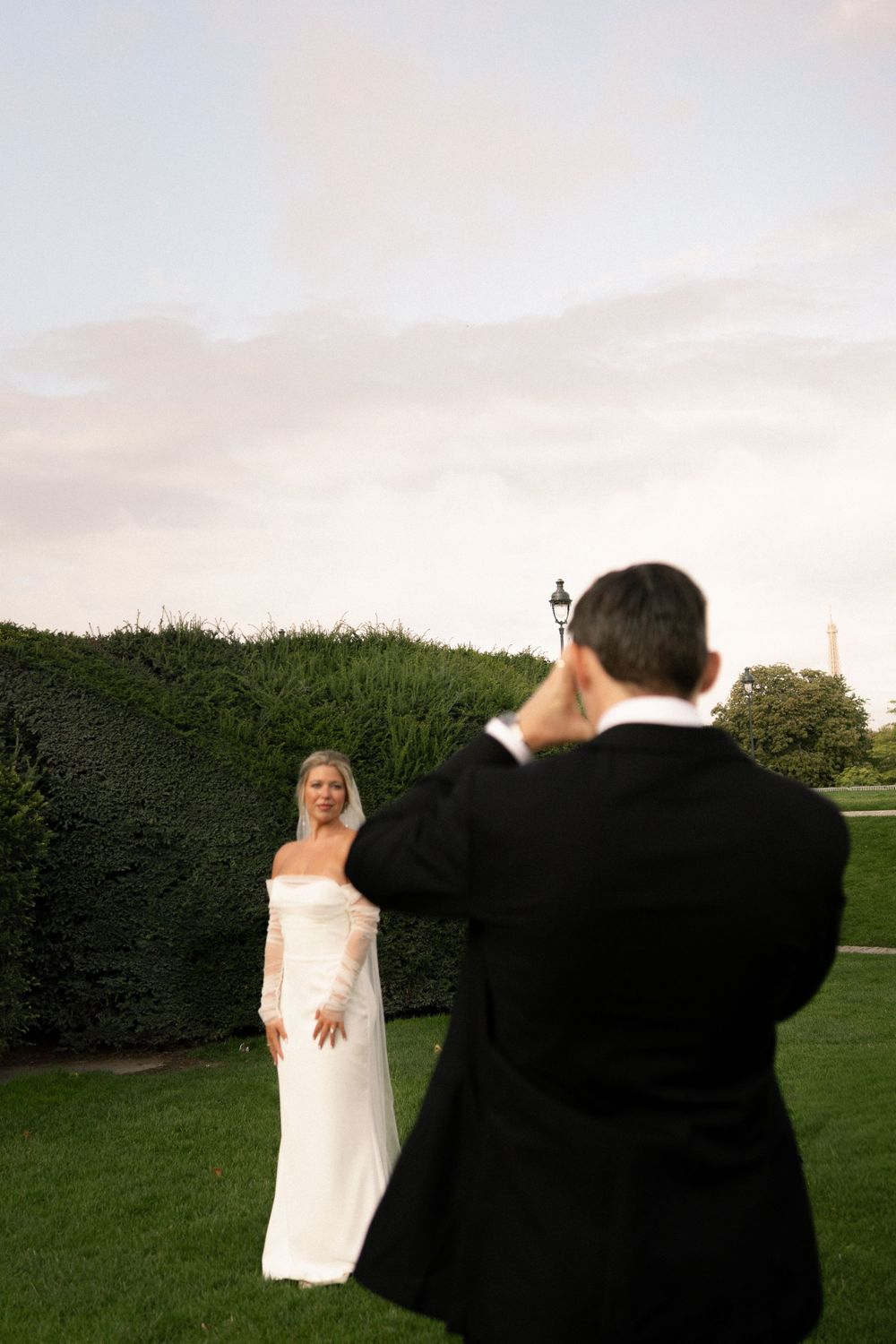 A photographer captures outdoor wedding portraits of a bride in a white dress against a scenic garden backdrop. Paris editorial elopement ph