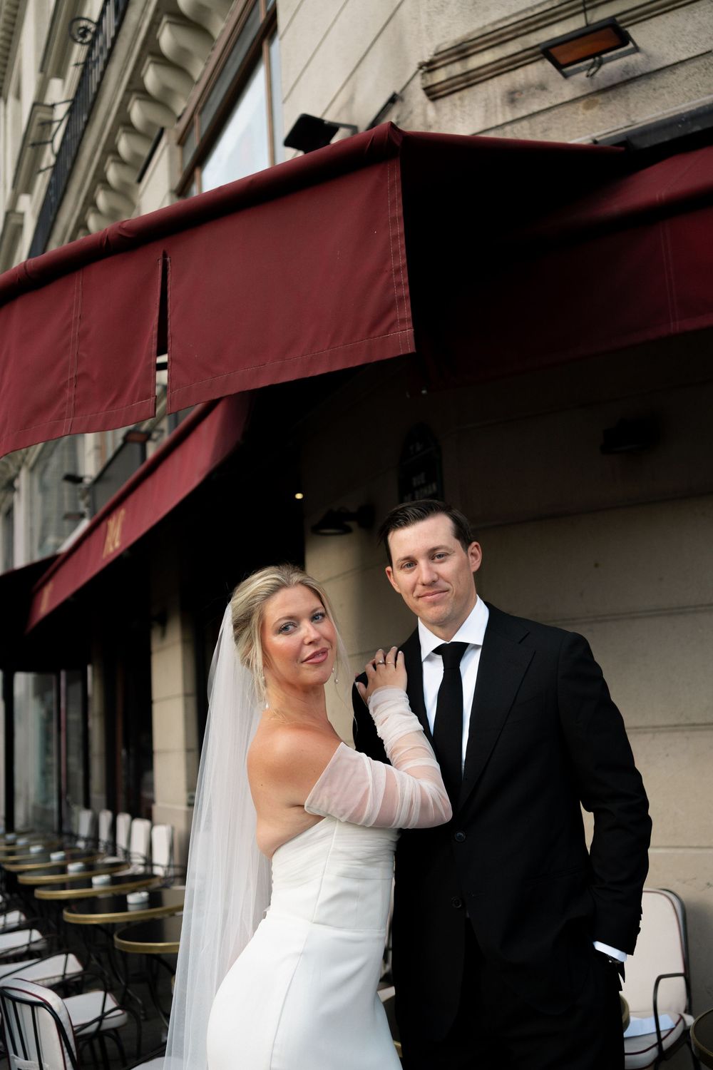 A bride and groom share a playful moment under a burgundy awning during their wedding photos. Paris editorial elopement photographer.