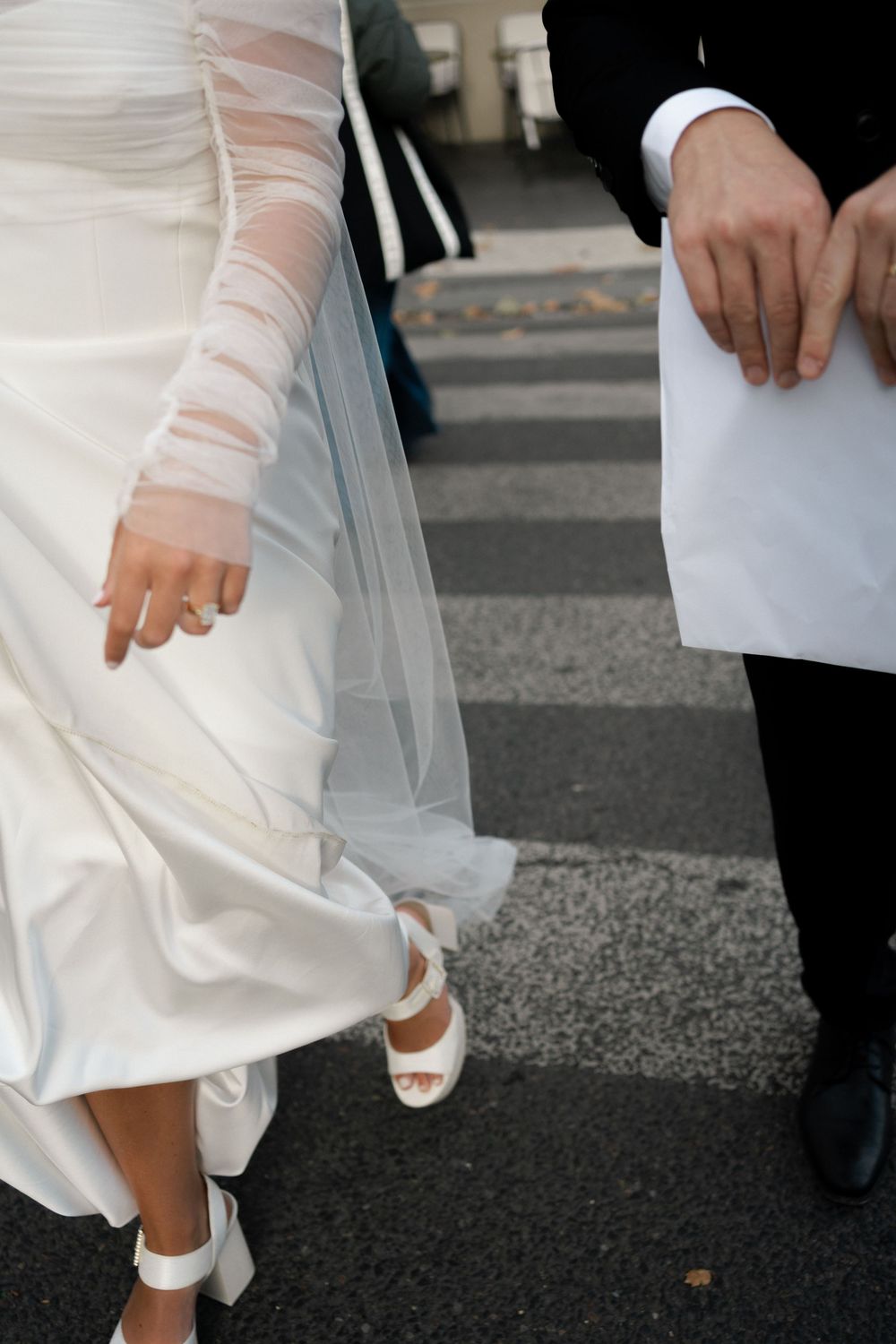 Close-up view of a white wedding dress and shoes walking on pavement. Paris editorial elopement photographer.