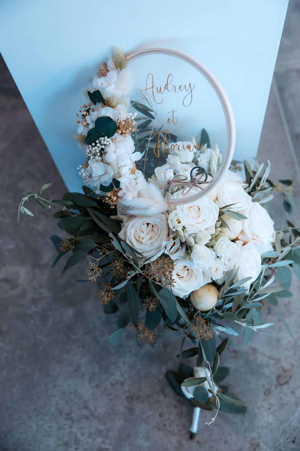 White and green floral wedding hoop with roses and eucalyptus against blue background.