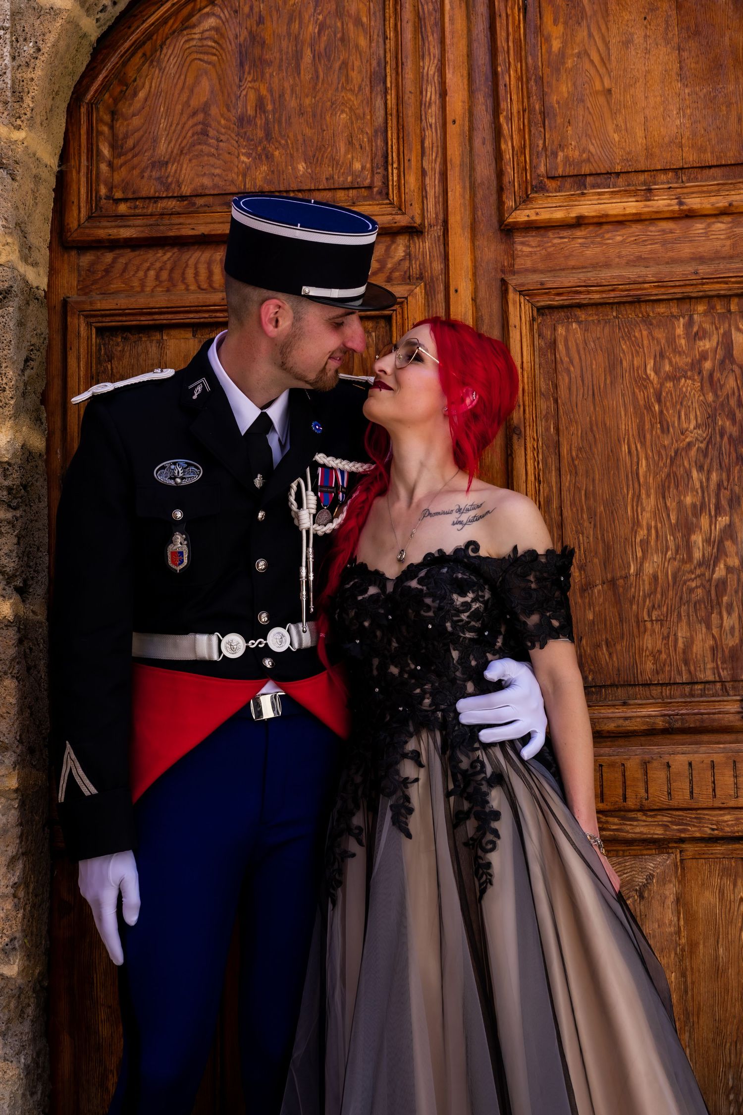 Romantic couple in military uniform and formal dress pose against wooden doors.