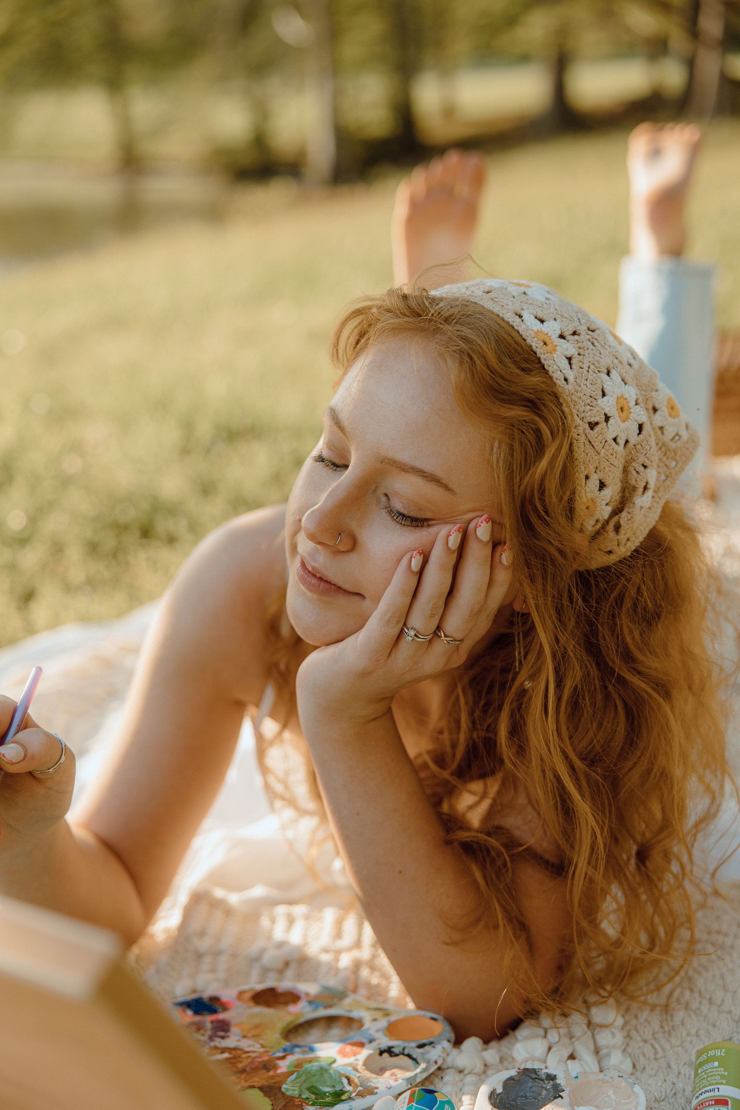Person in floral dress relaxing on a sunny picnic blanket outdoors.