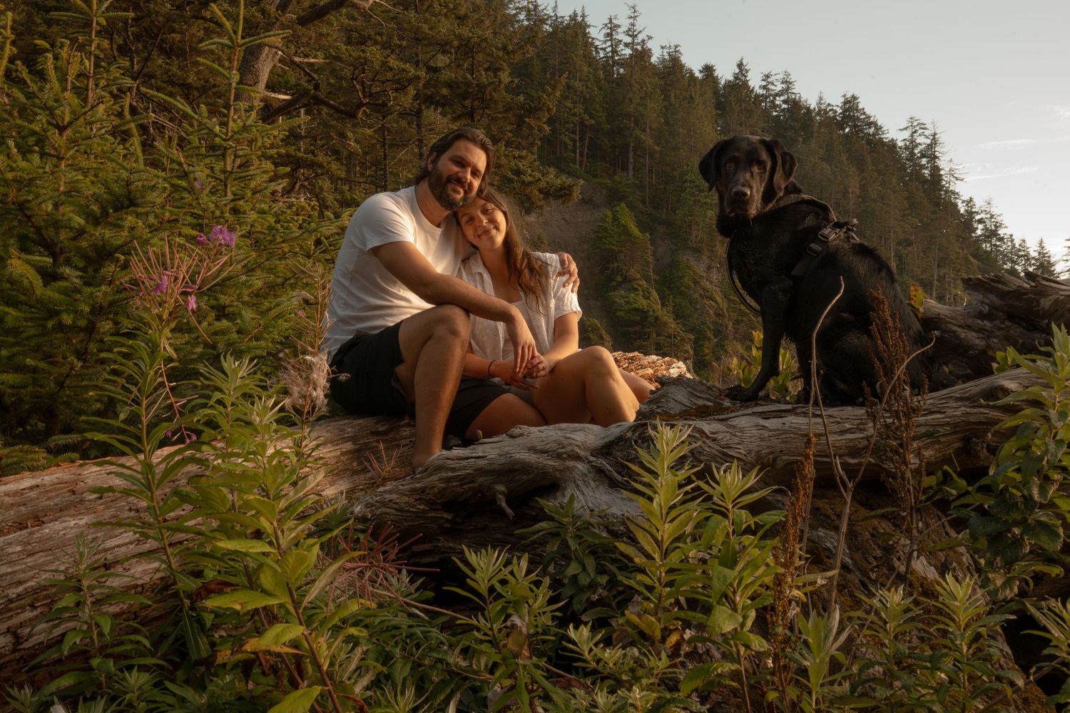 A young couple poses with their black lab during golden hour on short sands beach on the northern Oregon coast