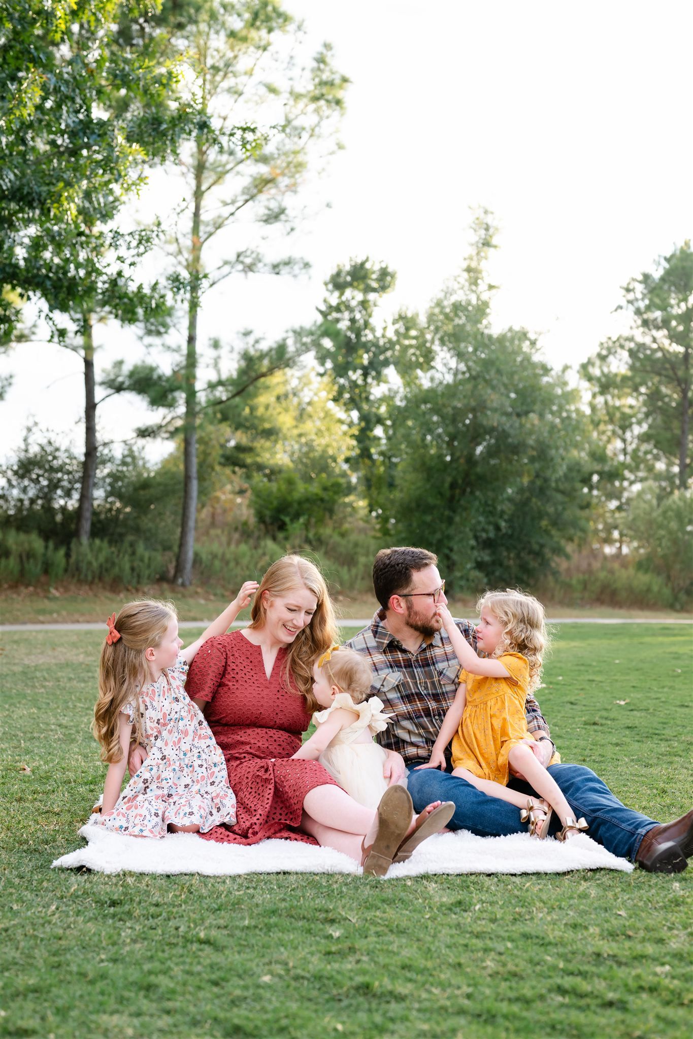 Family relaxing together on white blanket in grassy field during outdoor photo session.