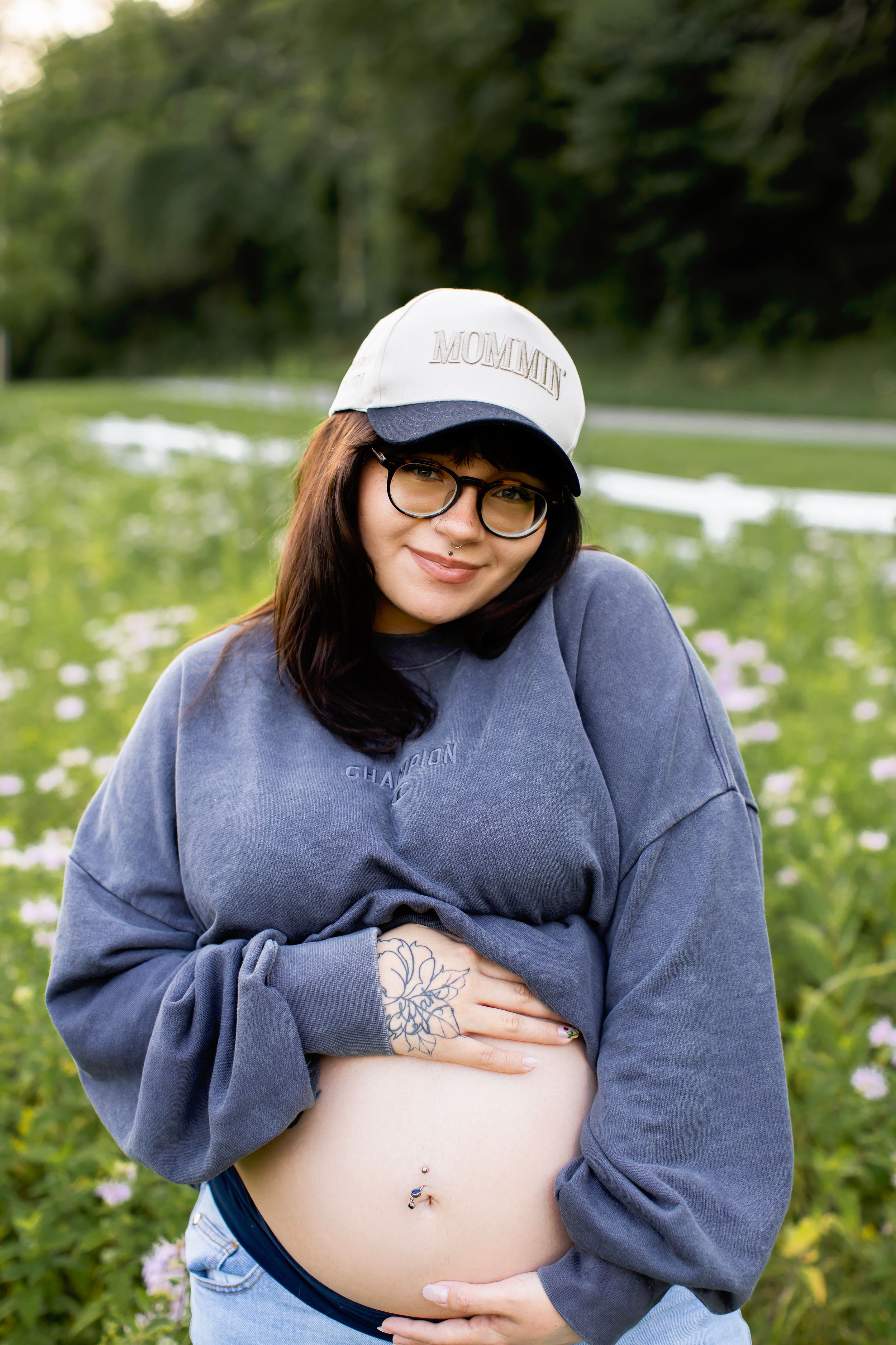 A series of maternity photos showing a pregnant belly in a blue sweater against a backdrop of white wildflowers.