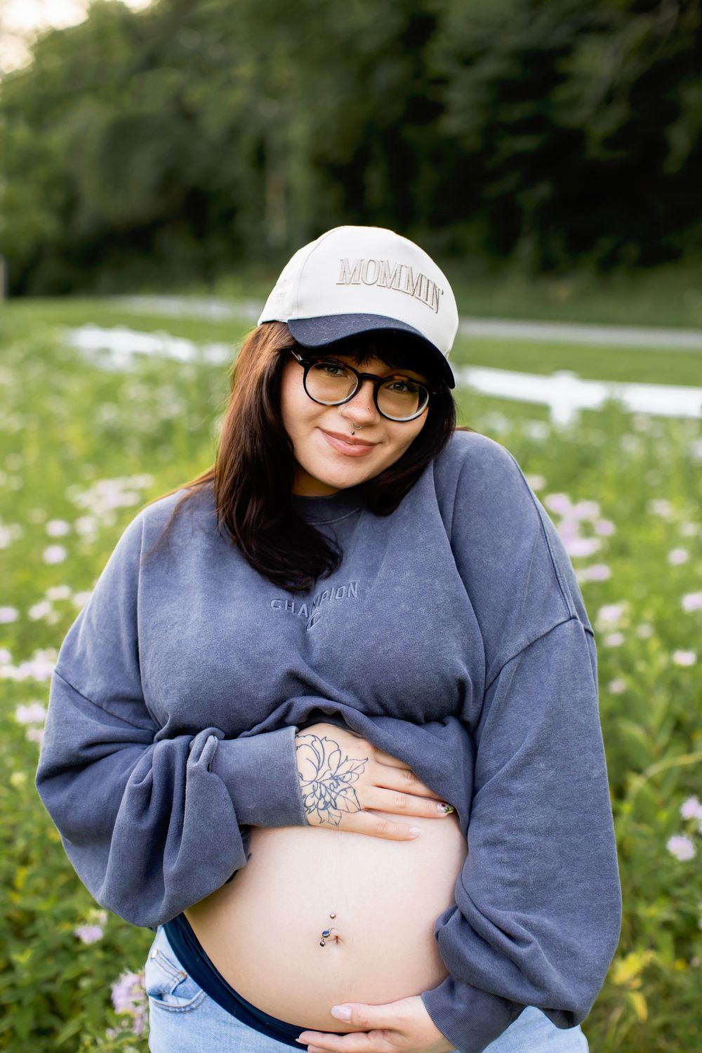 A series of maternity photos showing a pregnant belly in a blue sweater against a backdrop of white wildflowers.