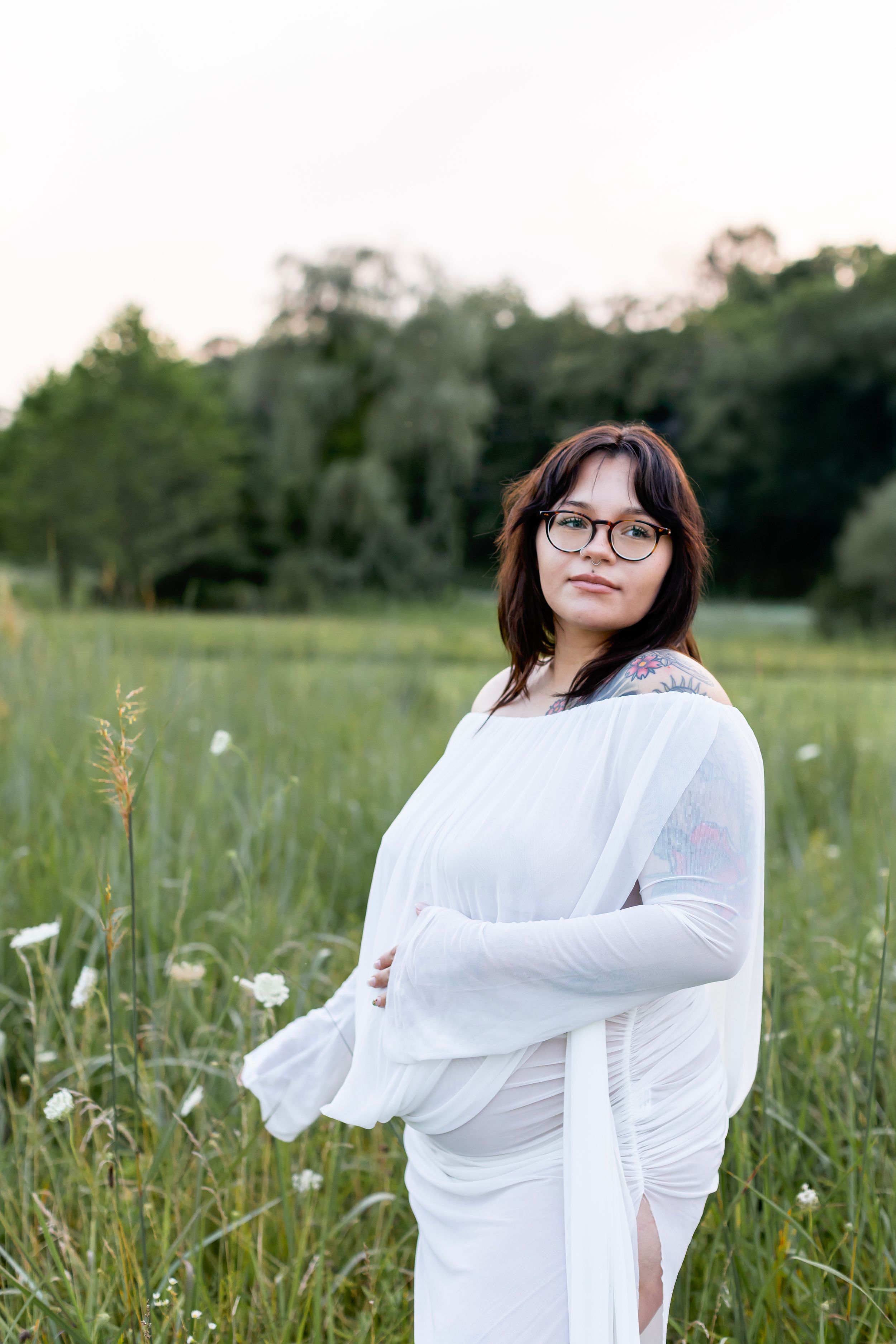 A person in a white dress poses gracefully in a serene meadow during golden hour.