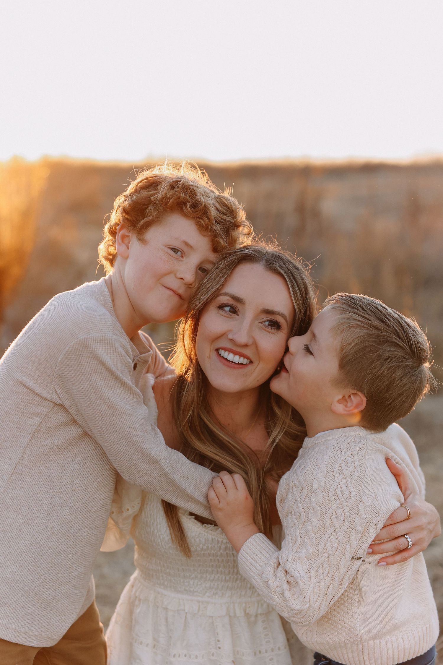 A family, mon and her two sons shares joyful moments together during a sunset photoshoot in a rustic outdoor field setting.