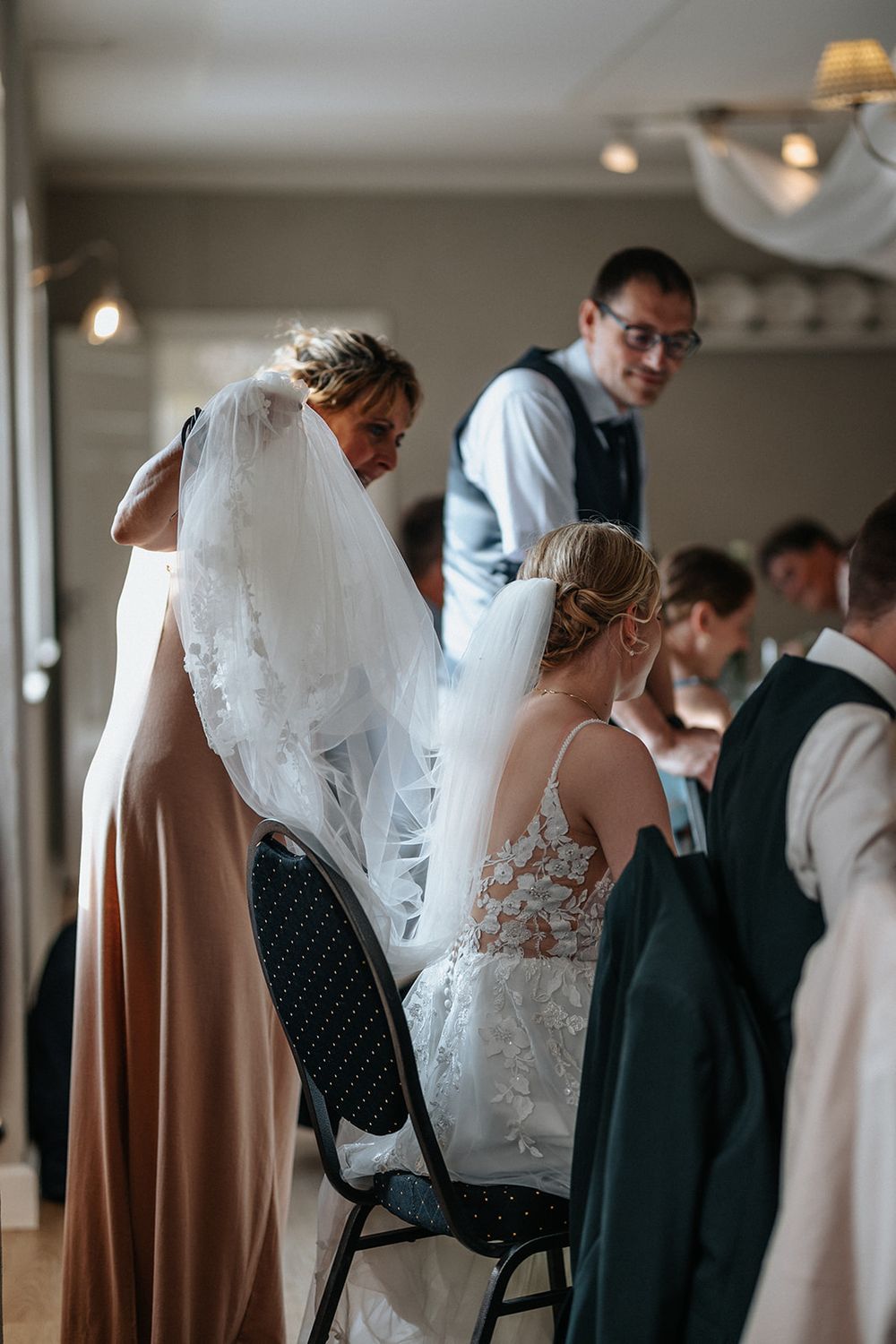 Wedding guests gather in a reception hall, with brides in white dresses and guests in formal attire mingling.