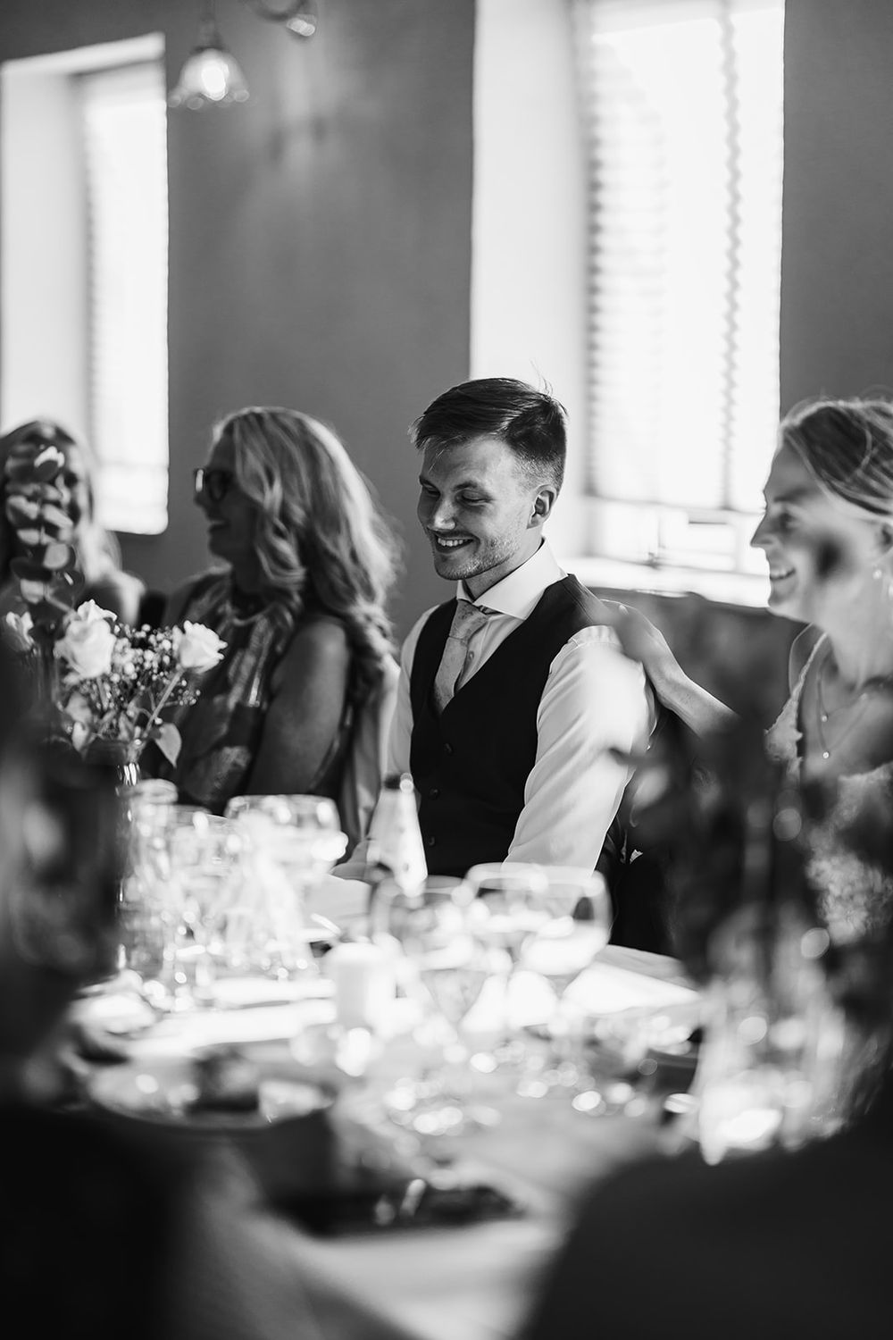 Black and white photograph of wedding guests seated at reception tables in an elegant dining room.