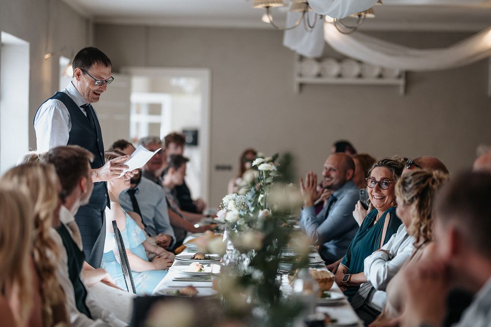 Wedding guests enjoy a festive reception dinner at decorated tables in an elegant indoor venue.