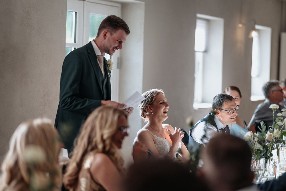 People gather in a bright room for a social event, with tables and chairs arranged along a wall.
