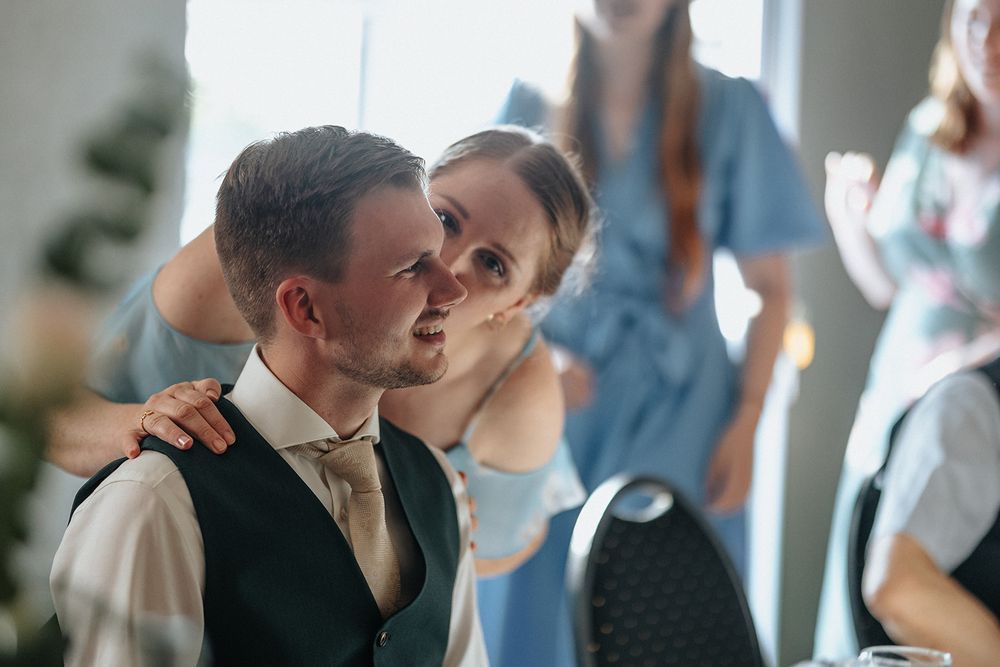 Two people share an intimate moment during a wedding celebration with guests in soft focus in the background.