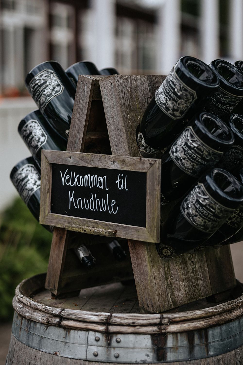 A series of rustic wooden signs with welcome messages in different languages sit atop vintage wine barrels.