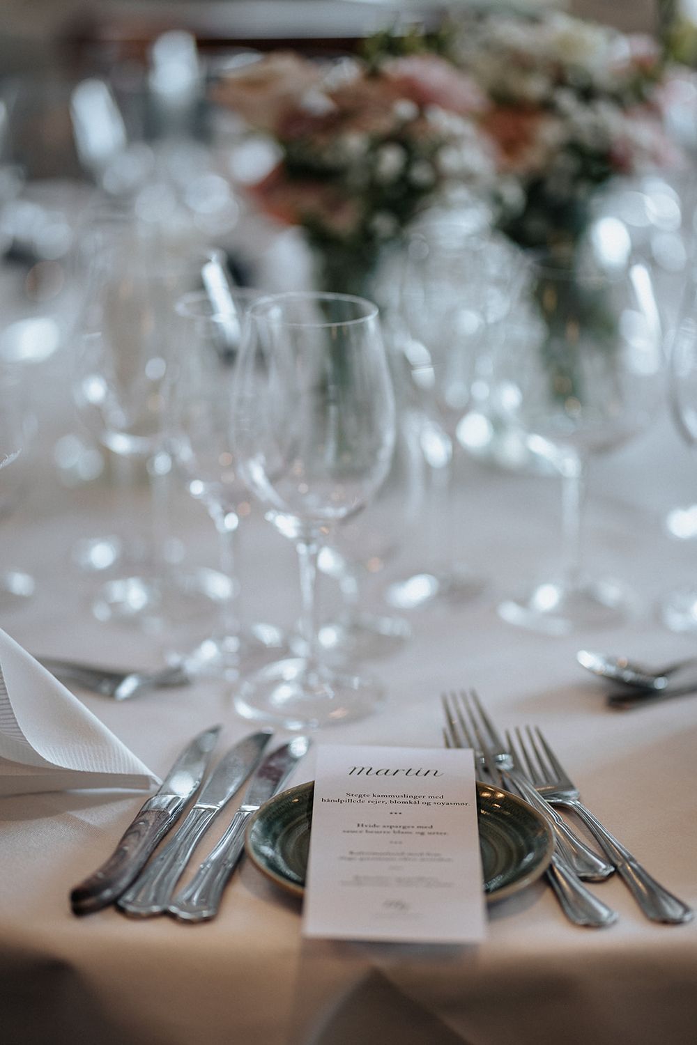 Elegant wedding table setting with silverware, place cards and floral decorations in soft focus at a formal reception.