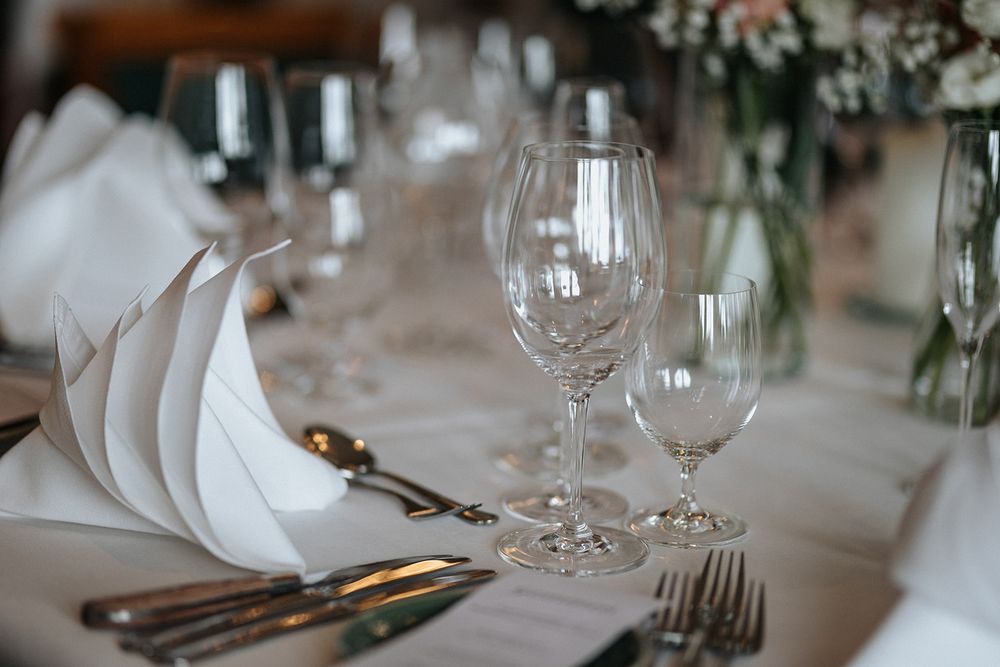 Elegant table settings with wine glasses and cutlery arranged on white tablecloths for a formal dining event.