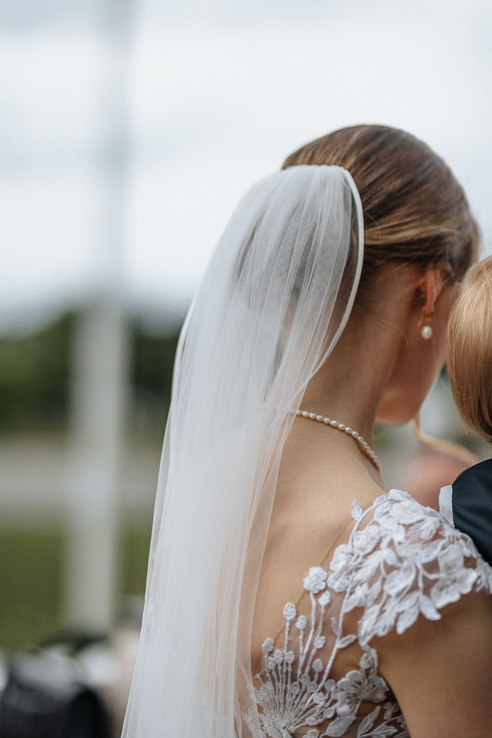 Close-up details of a bride's veil and pearl earrings against a soft blurred background.