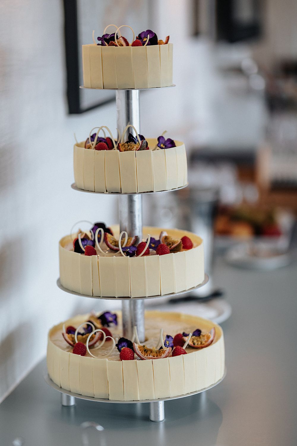A three-tiered white wedding cake decorated with colorful chocolate-covered strawberries on a silver stand.