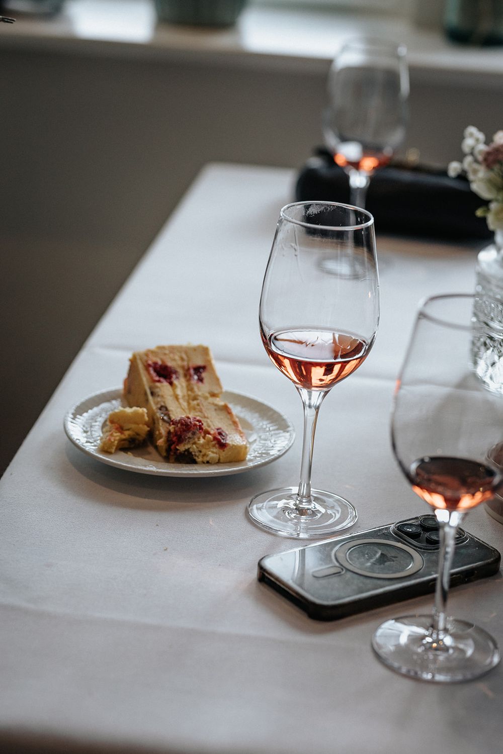 A glass of rosé wine and a sandwich on a white plate sit on an elegant dining table with a smartphone nearby.