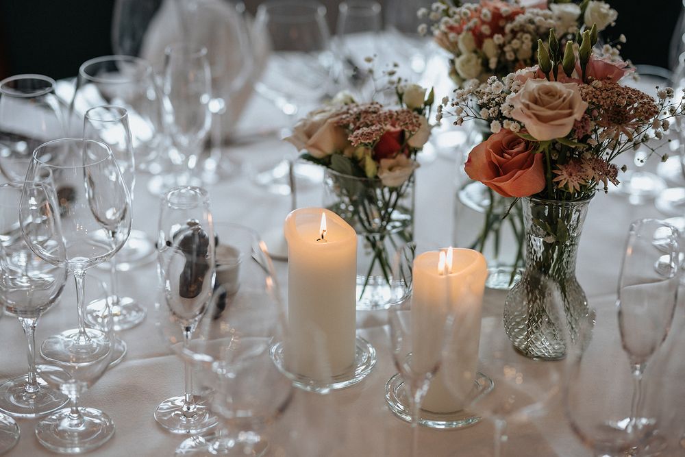 Elegant wedding table setting with soft candlelight and delicate floral arrangements in glass vases along a white tablecloth.