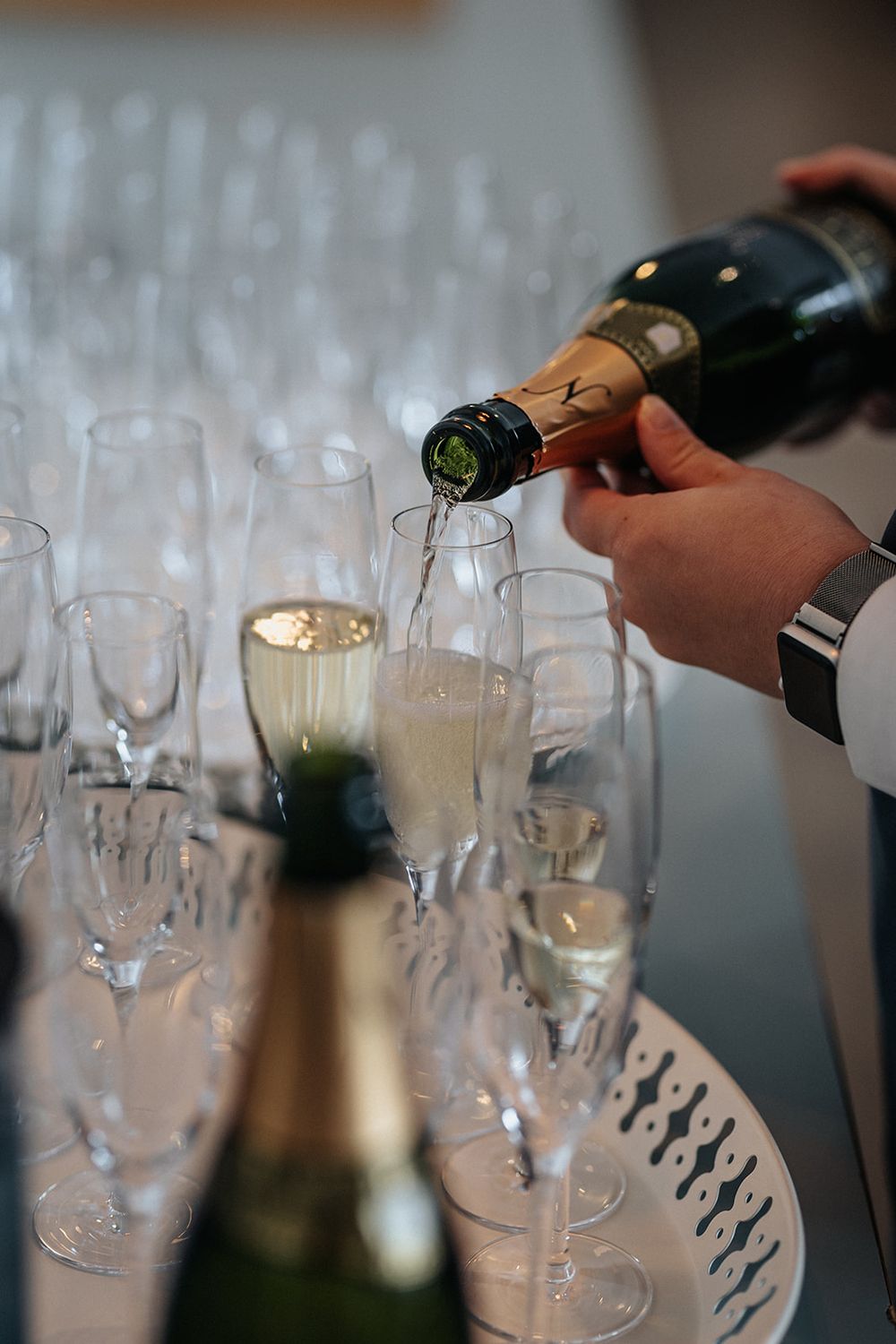 Hands pouring champagne into elegant crystal flutes arranged in a row at a formal event setting.