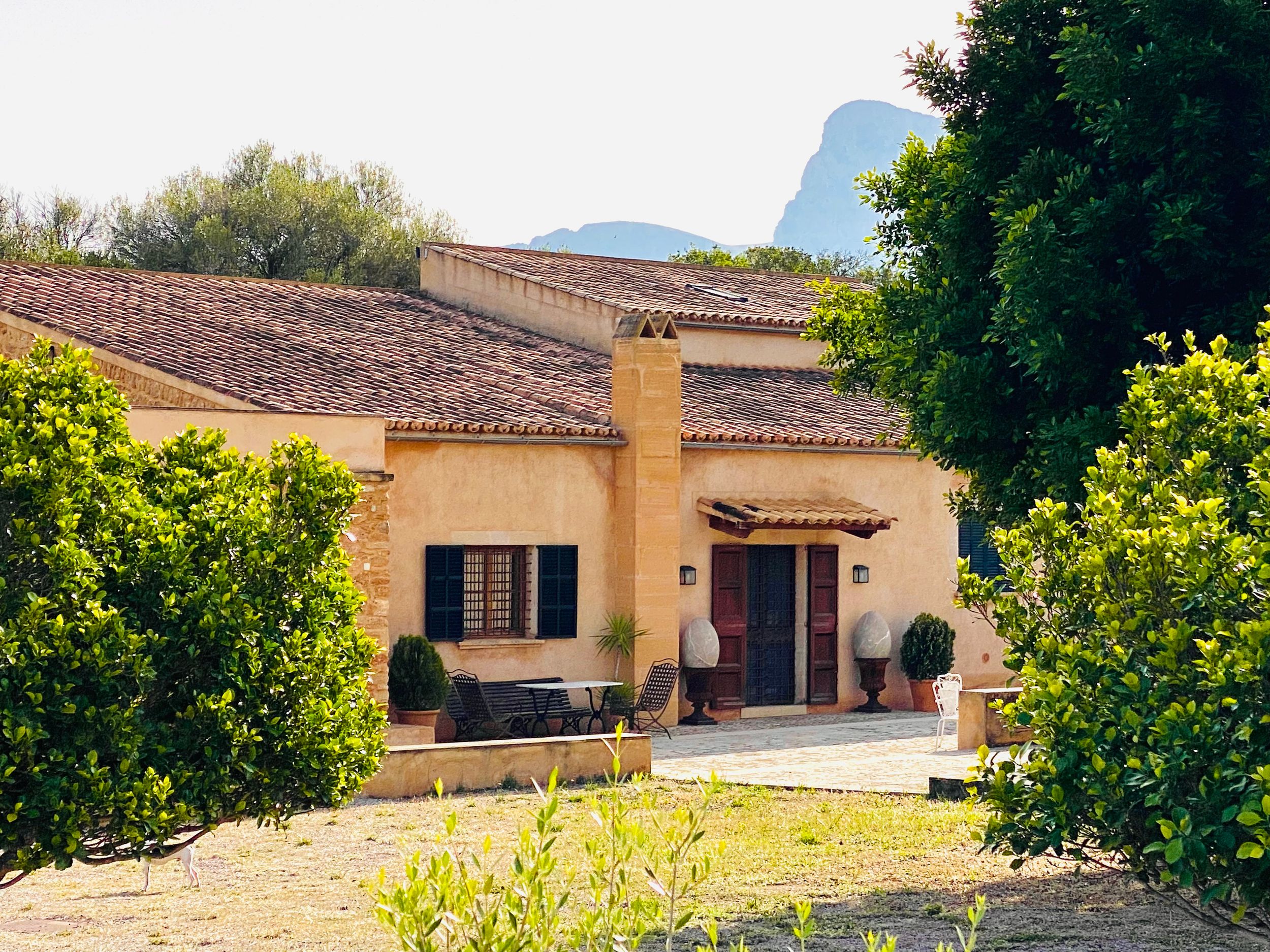 Panoramic view of a Mediterranean style villa with terracotta roof tiles and lush landscaping in a sunny setting.