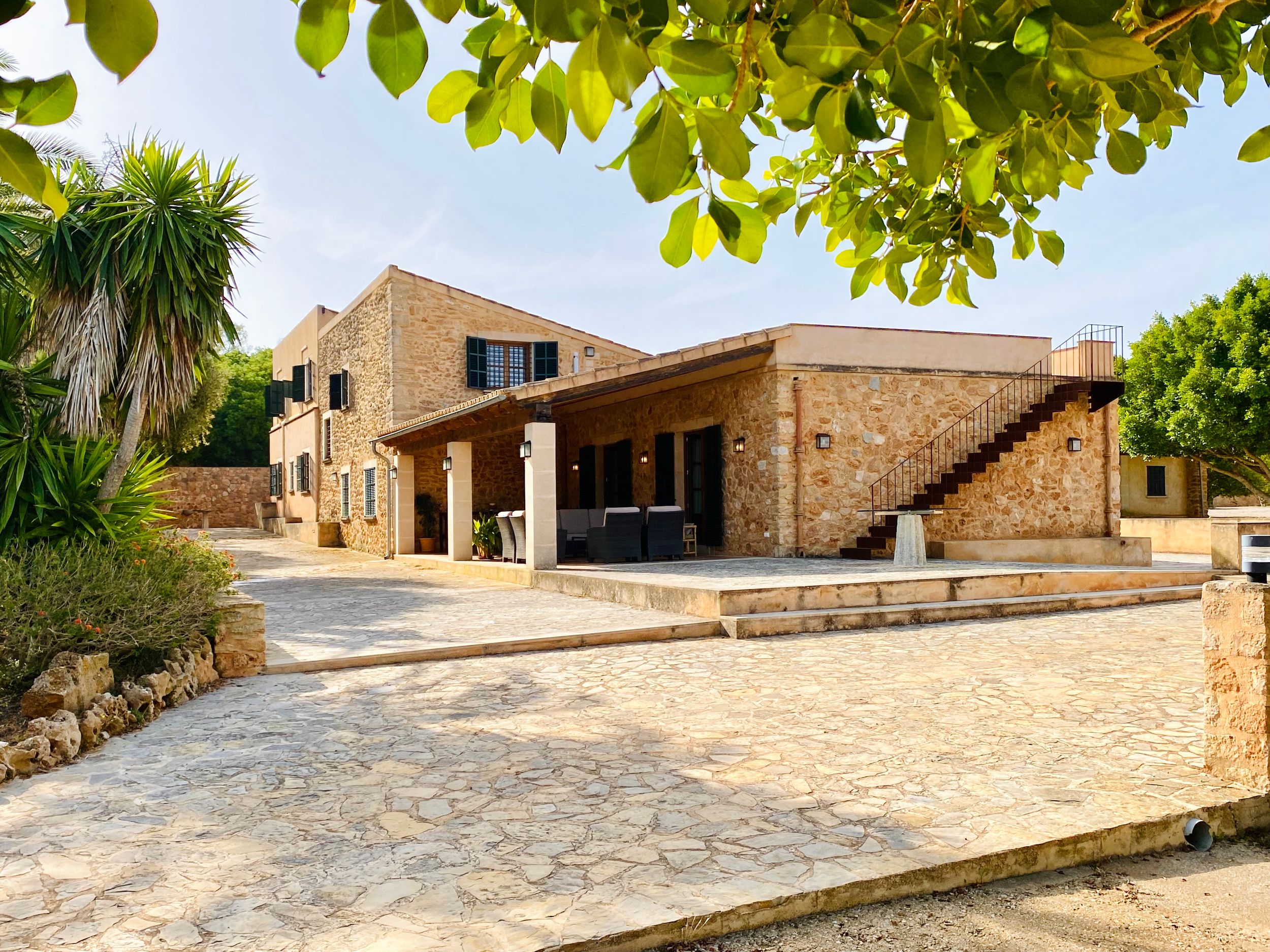 A series of connected stone buildings with green foliage overhead create a rustic Mediterranean architectural scene.