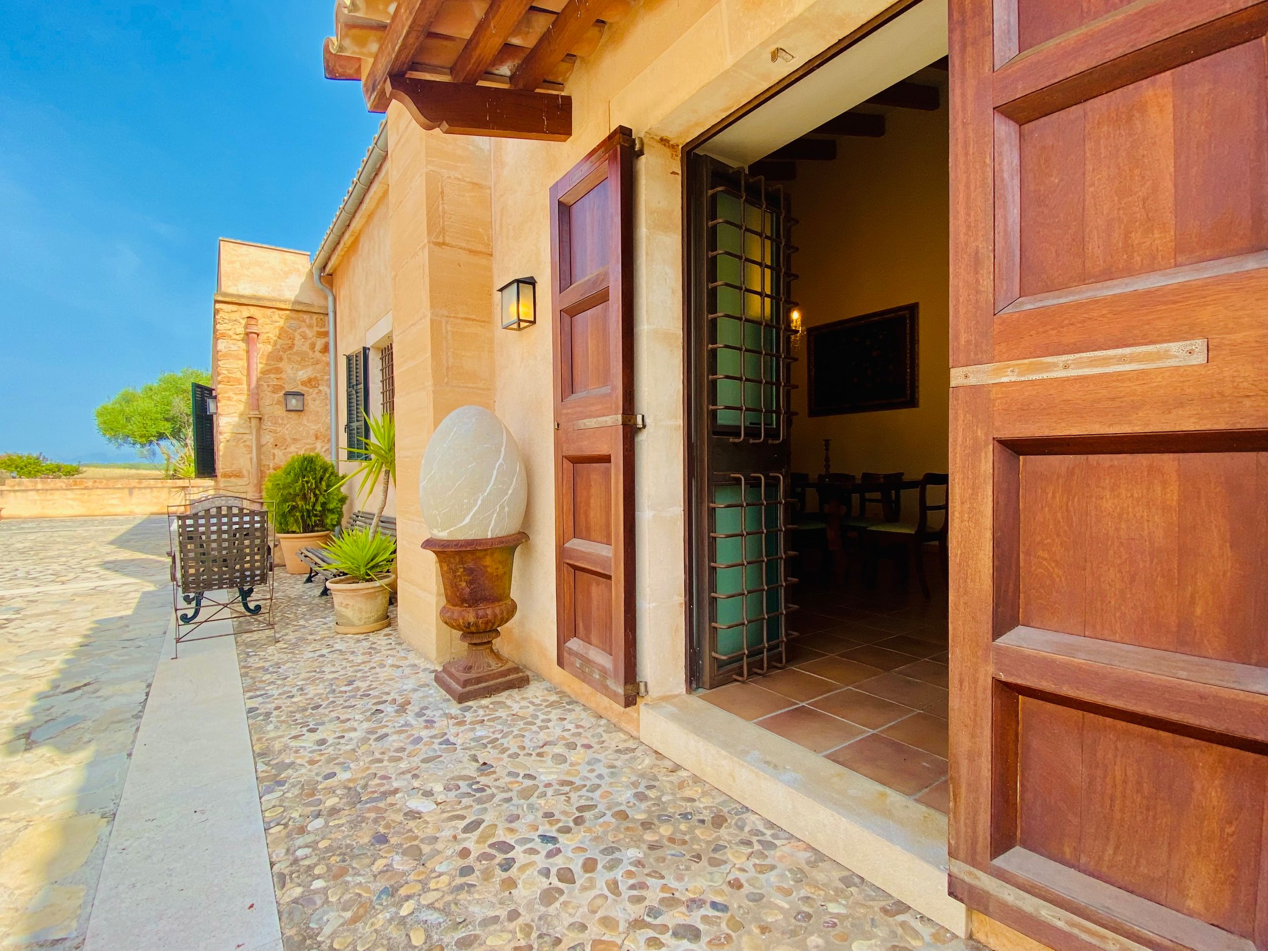 Rustic stone walkway with terracotta walls and wooden beams leads through a Mediterranean-style courtyard.