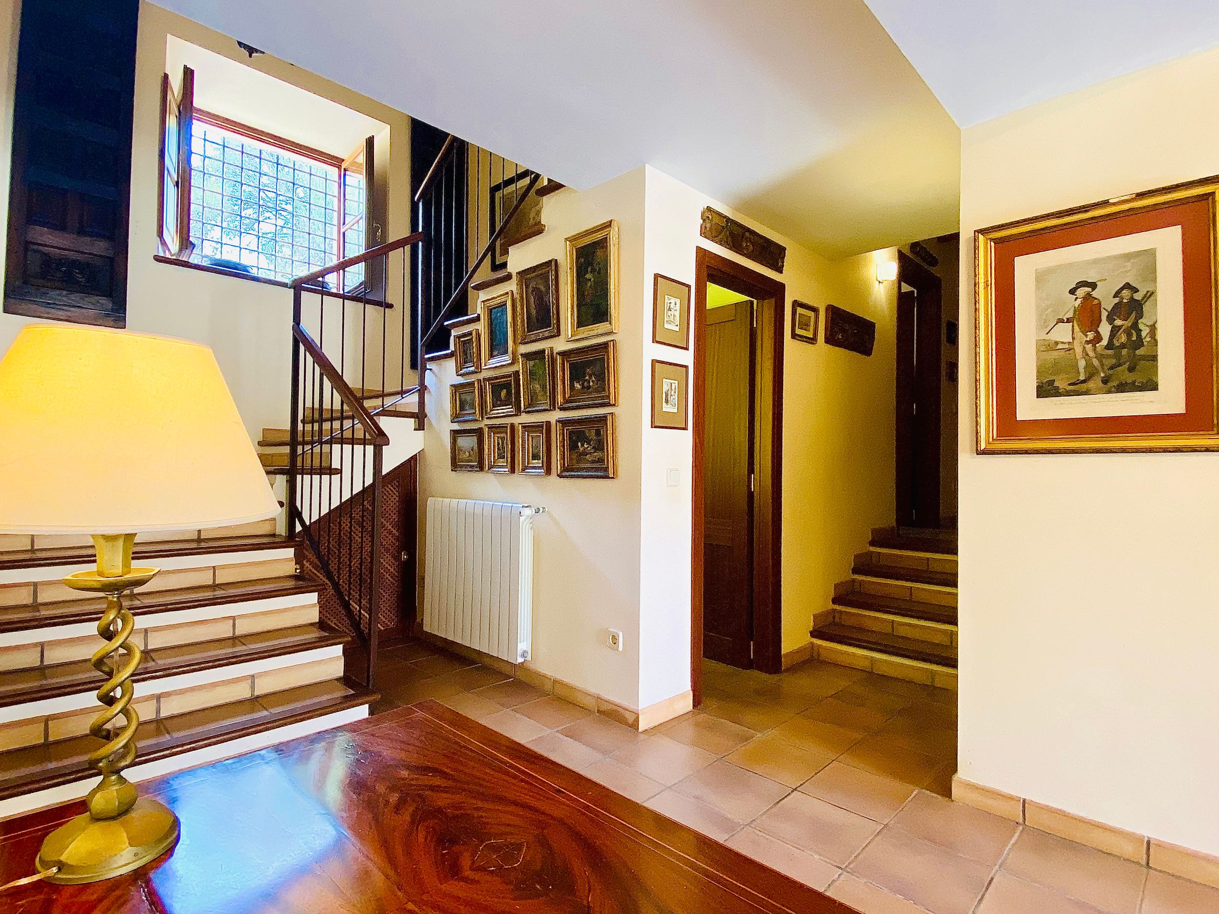 Interior hallway with wooden spiral staircase, yellow walls, framed artwork, and built-in bookshelves in a residential space.