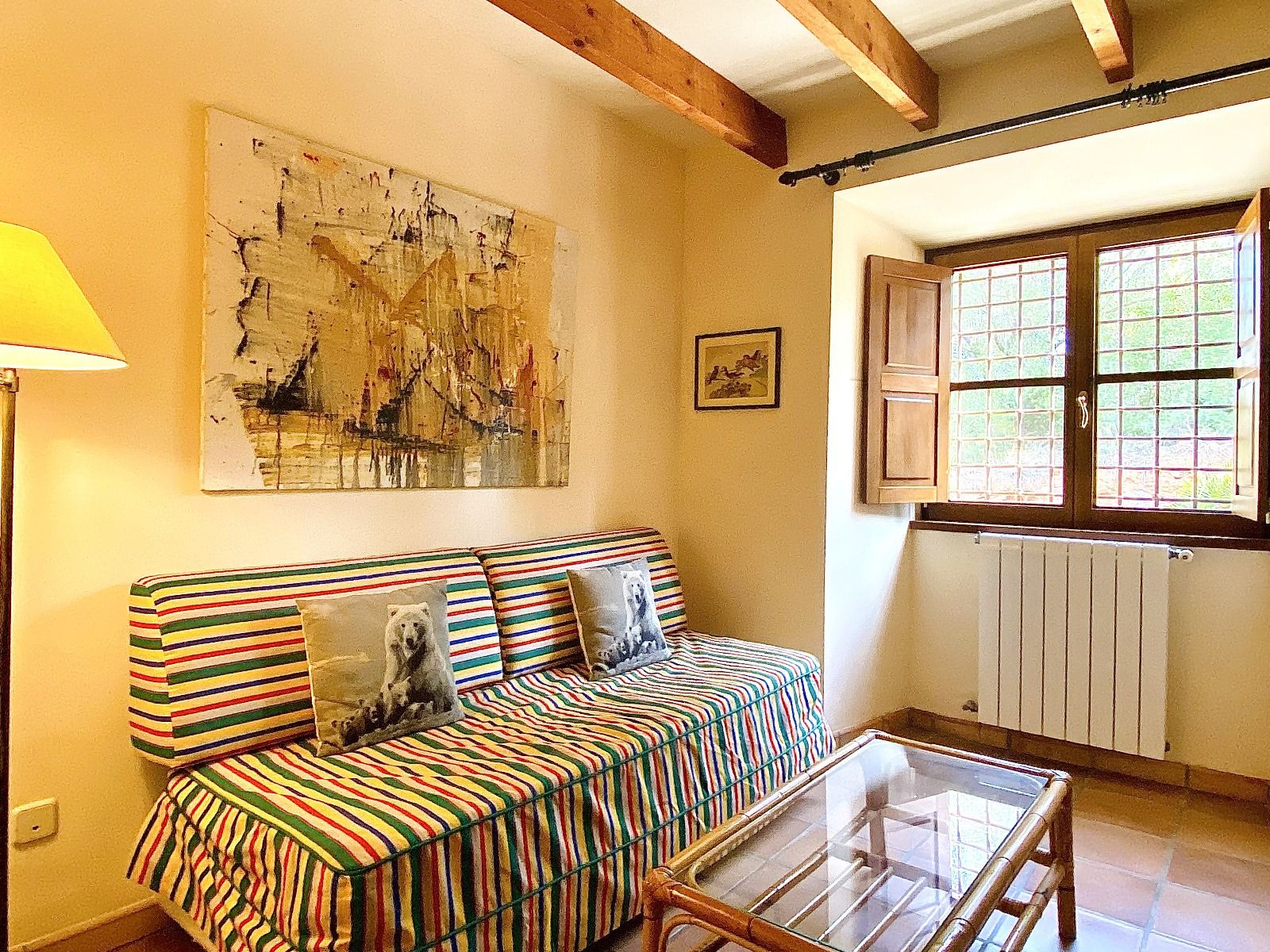 Cozy bedroom interior with striped bedding, wooden beams, and natural light streaming through windows.