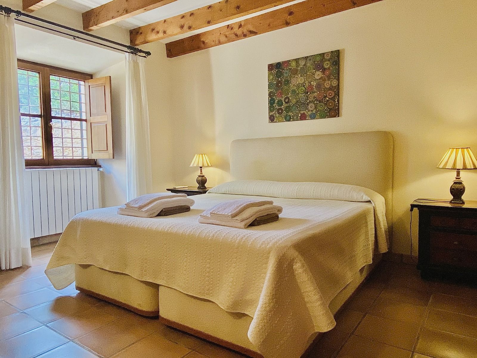 Cozy rustic bedroom with exposed wooden beams, white bedding, and warm lighting creates an inviting atmosphere.