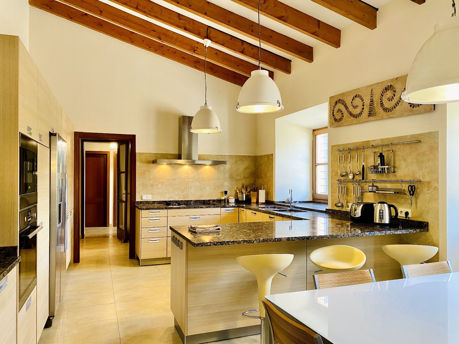 Modern kitchen interior with exposed wooden beams, granite countertops, and pendant lighting in a Mediterranean style home.