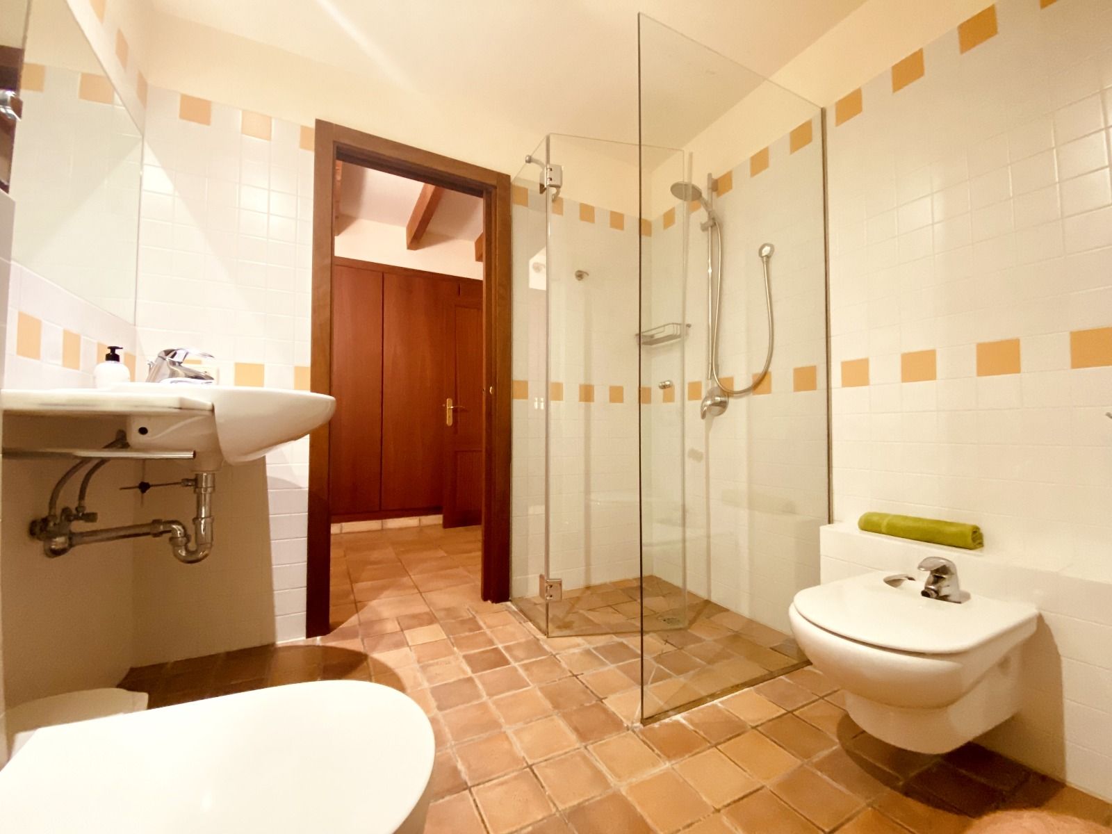 Modern bathroom interior with terra cotta floor tiles, glass shower enclosure, and warm lighting fixtures.