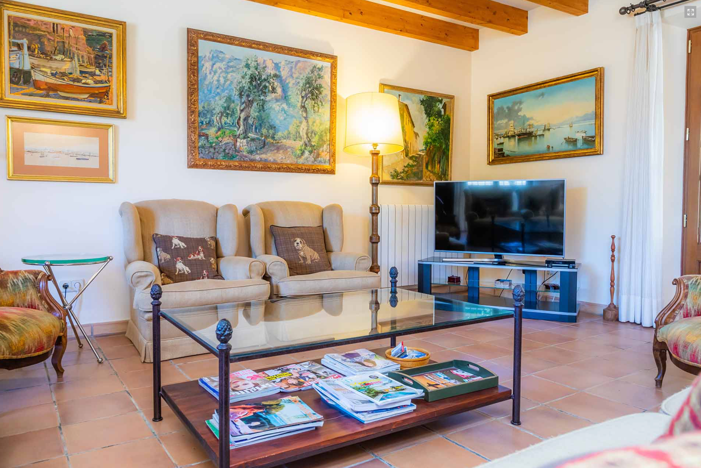 A long gallery room with exposed wooden beams features multiple framed artworks and comfortable seating arrangements.