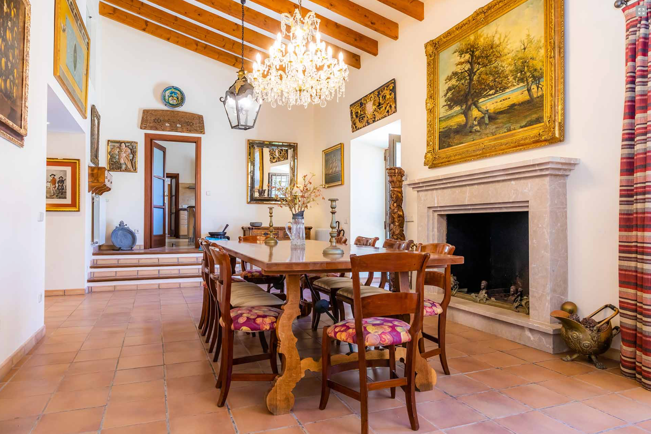 Elegant dining room with exposed wooden beams, crystal chandelier, and traditional decor featuring white walls and artwork.