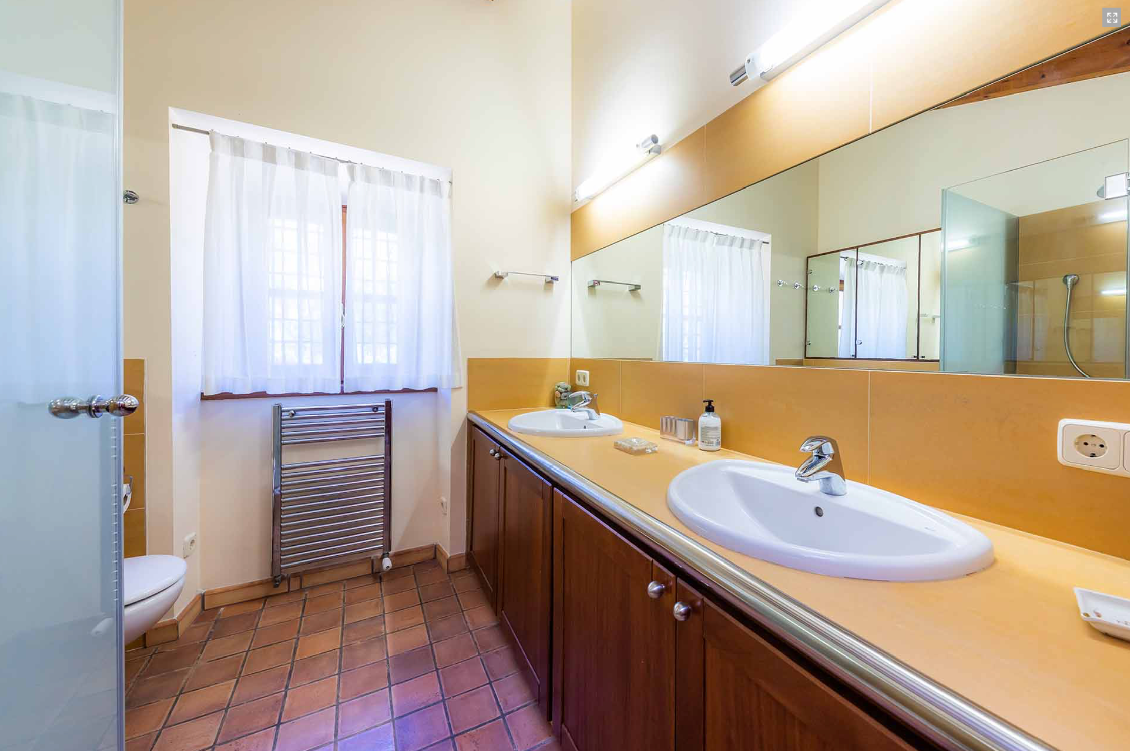 Modern bathroom interior with beige walls, large mirror, white sink and wood cabinets in luxury apartment.