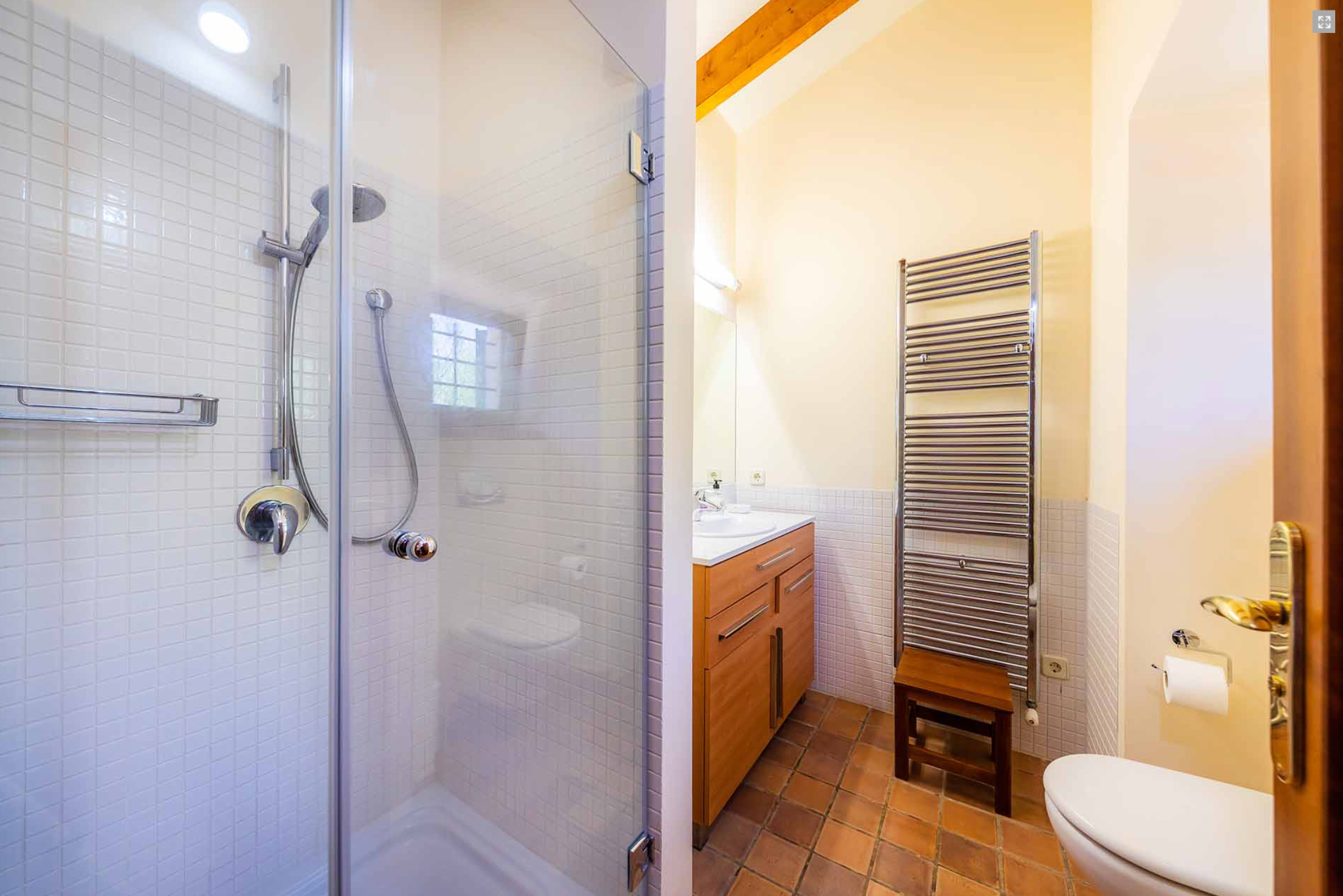 Modern bathroom interior with white tile walls, glass shower enclosure, and chrome towel warmer mounted on wall.