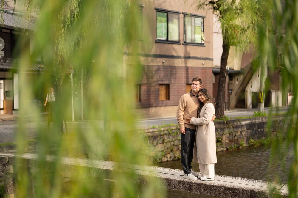Couple embracing near a peaceful canal framed by weeping willow branches in Kyoto, Japan.