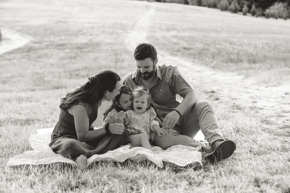 A black and white photo of a happy family of four sitting together on a blanket in a grassy field.