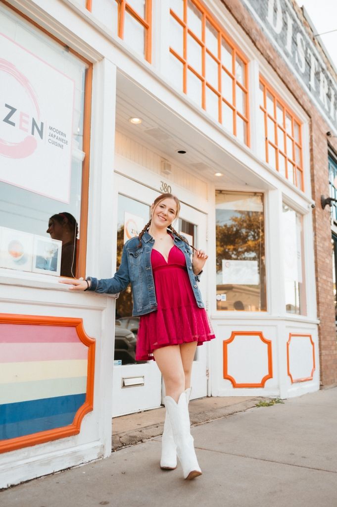 A fashion shoot outside a storefront featuring a red dress, denim jacket and white cowboy boots.