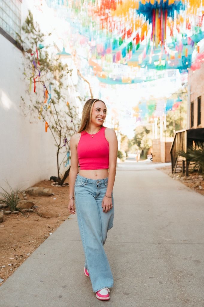 A casual outfit featuring wide-leg jeans and a red tank top under colorful hanging papel picado banners.
