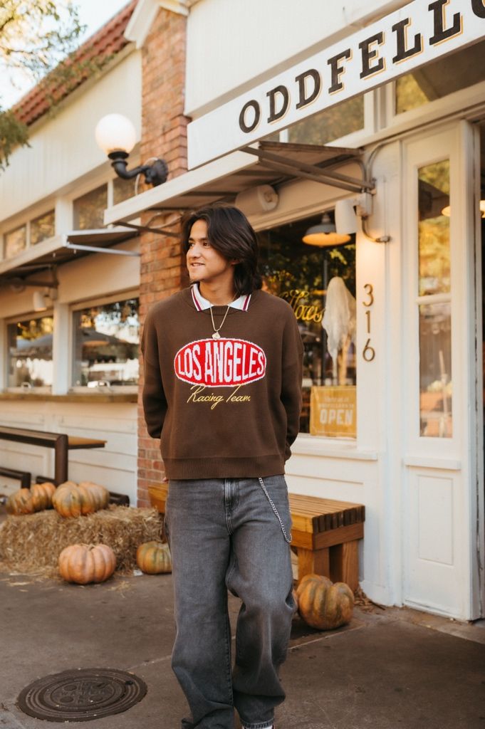 Brown Los Angeles sweatshirt and jeans shown against storefront with autumn pumpkin decorations.