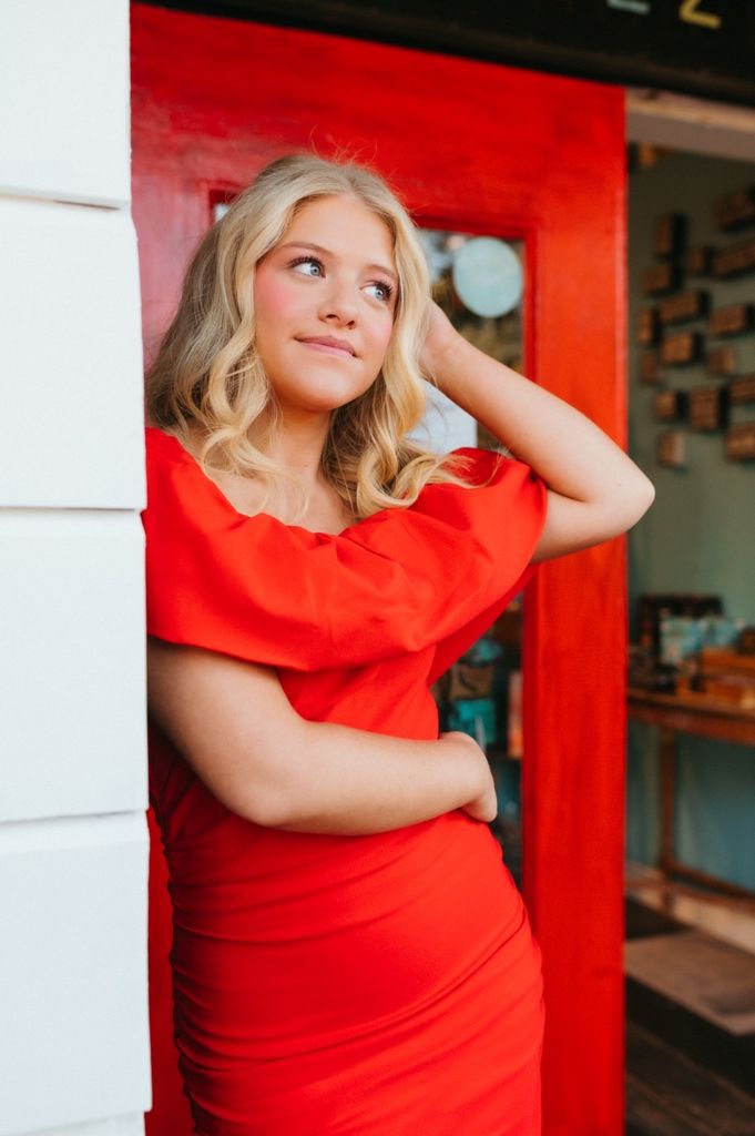 Woman in vibrant red dress poses against red backdrop in artistic portrait series.