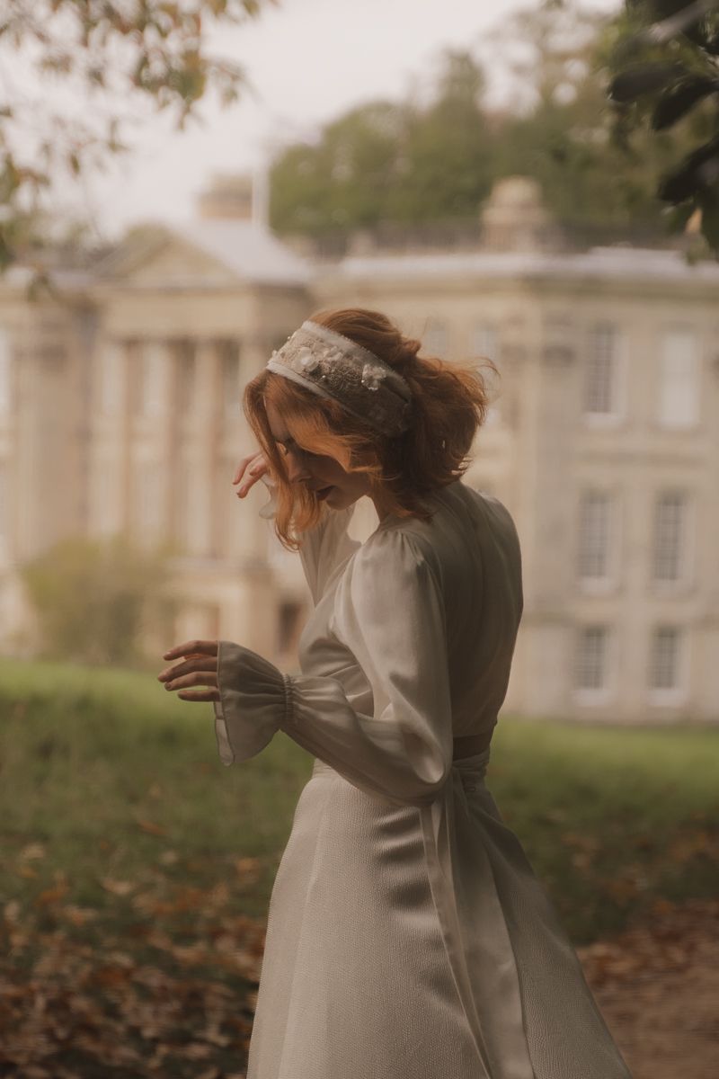A person in a white dress spins gracefully among fallen autumn leaves near a grand historic building.