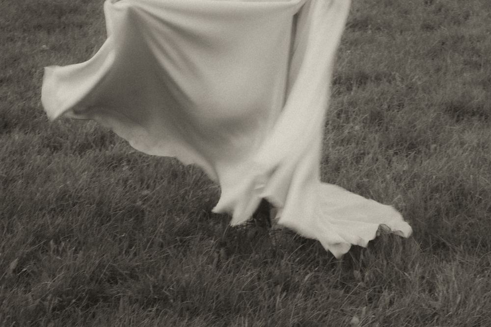 A flowing white wedding dress twirls in motion against a dark grass background creating an ethereal effect.
