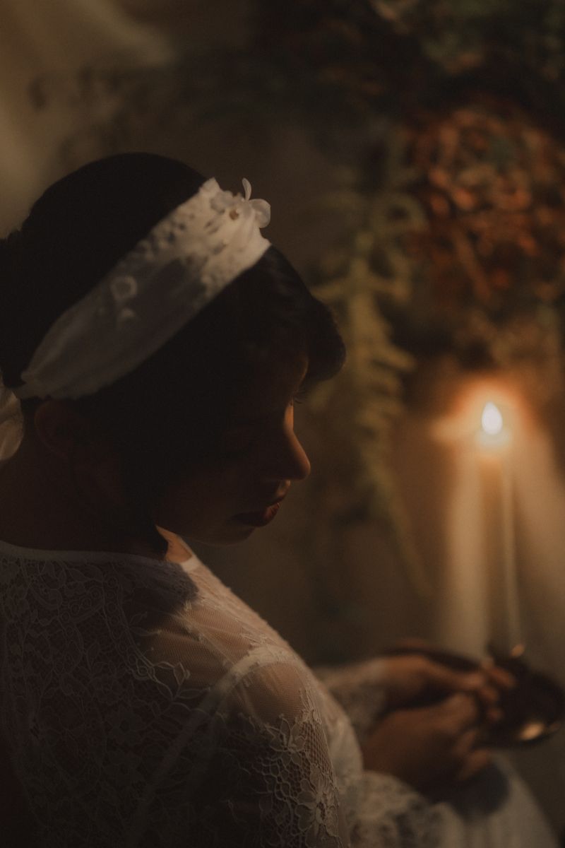A moody artistic photo of a white cat illuminated by warm candlelight against a dark background.