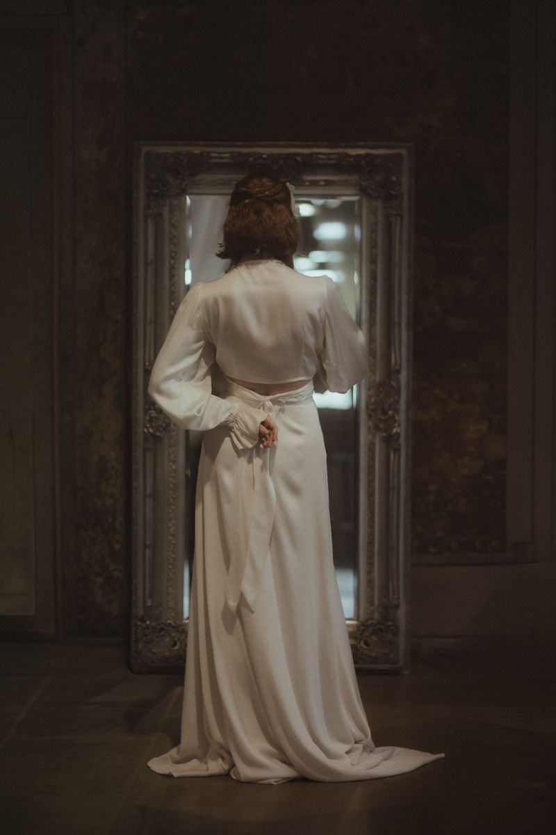 A figure in a flowing white dress moves dramatically through a dark, atmospheric hallway with arched doorways.