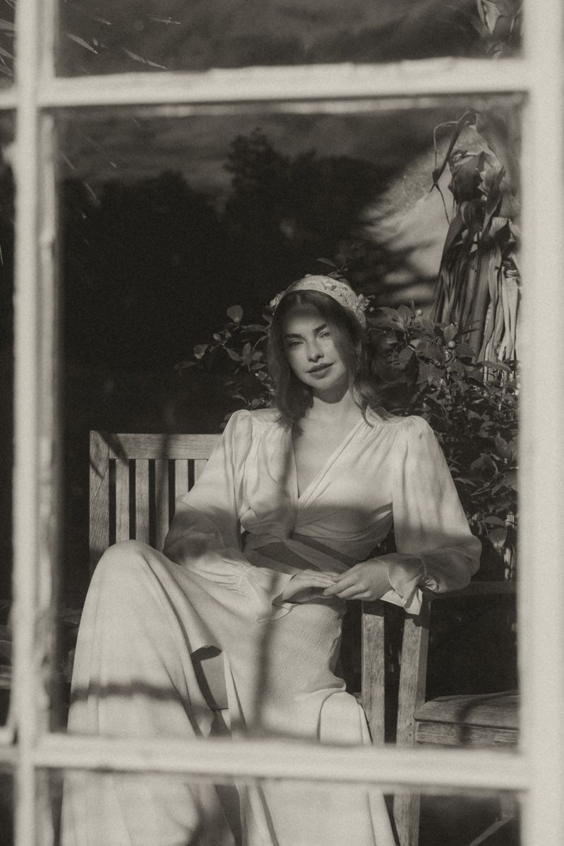 A vintage black and white photograph showing people in white dresses sitting on a porch in a casual summer setting.